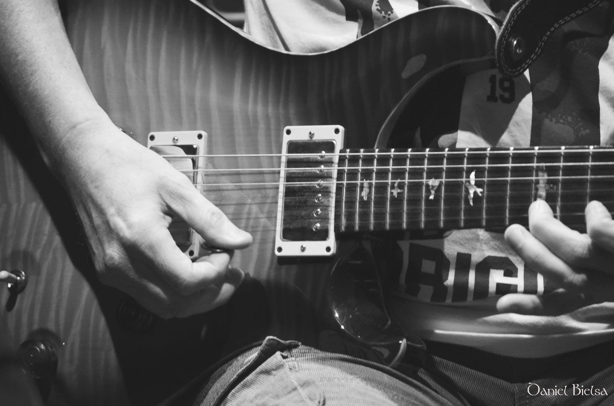 Schwarz-weiße Nahaufnahme von Händen, die eine E-Gitarre mit Vogel-Inlays auf dem Griffbrett spielen.